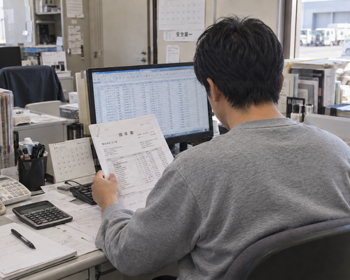 請求書とパソコンを確認しながら作業する男性の後ろ姿