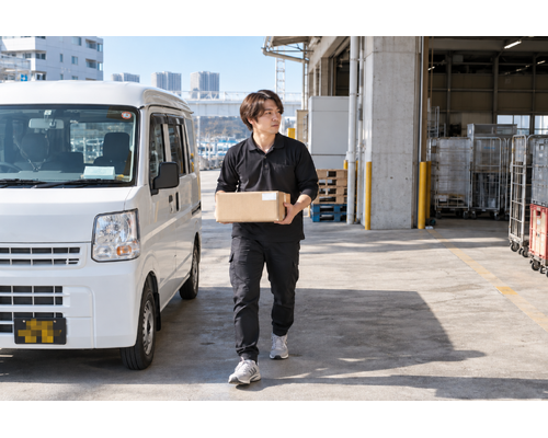 軽バンのそばで荷物を運ぶドライバー