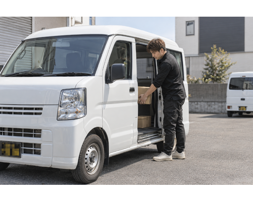白い軽バンのそばで配送の準備をするドライバー