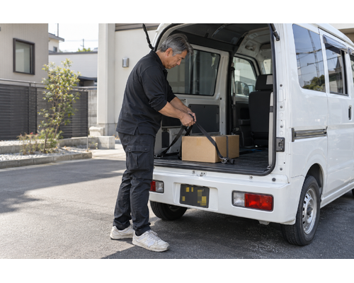 白い軽バンのそばで配送の準備をするドライバー