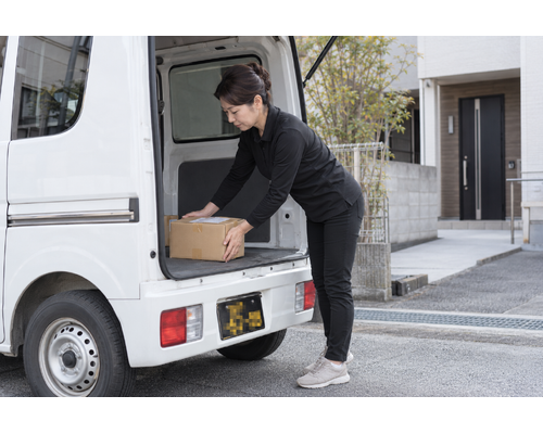 白い軽バンのそばで配送の準備をするドライバー