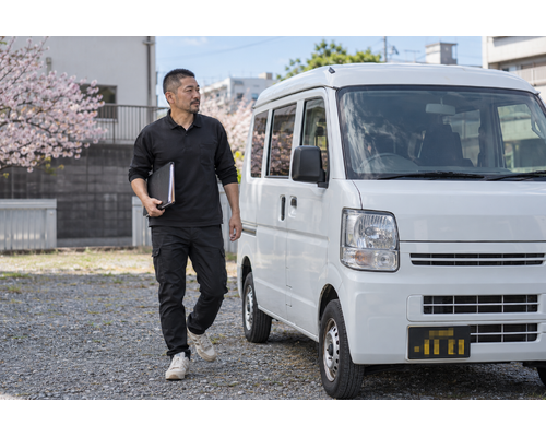 白い軽バンのそばで書類を持つドライバー