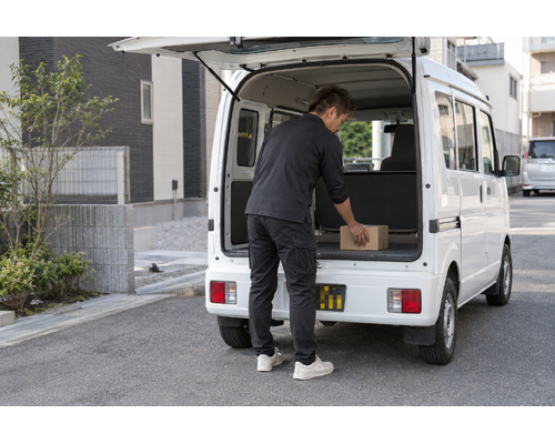 白い軽バンのそばで配送の準備をするドライバー