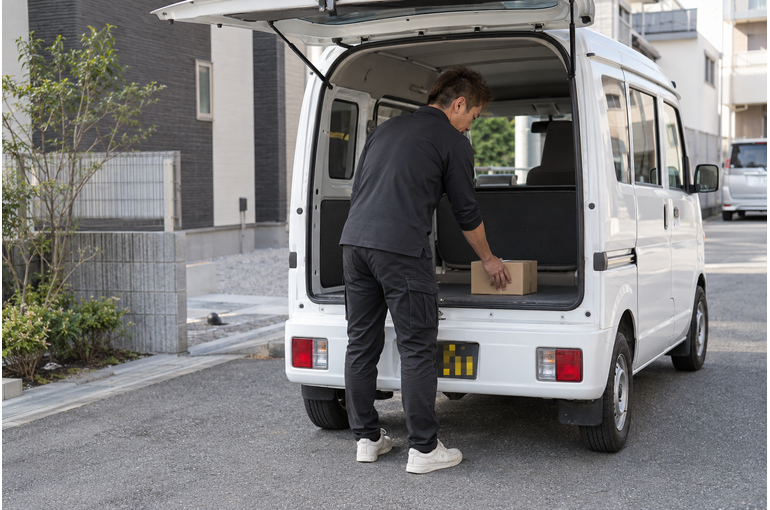 白い軽バンのそばで配送の準備をするドライバー