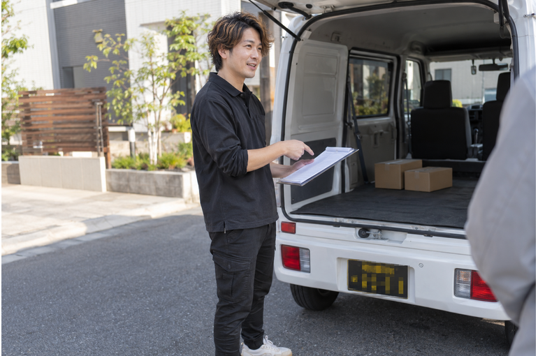 白い軽バンのそばで配送の準備をするドライバー