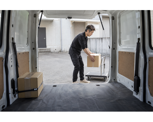 軽バンの荷室から見た、荷物を台車へ移す男性ドライバー