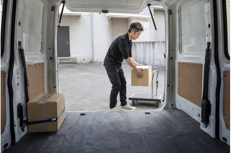 軽バンの荷室から見た、荷物を台車へ移す男性ドライバー