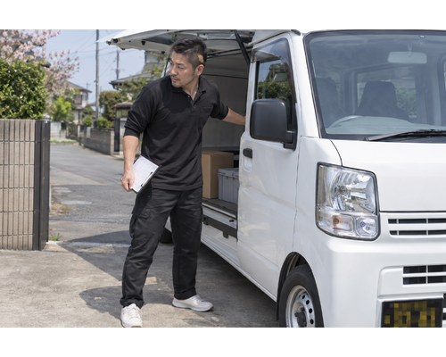白い軽バンのそばで配送作業をするドライバー