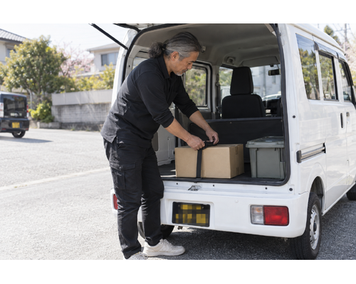 白い軽バンのそばで配送作業をするドライバー