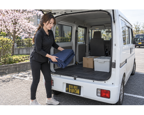 白い軽バンのそばで配送作業をするドライバー