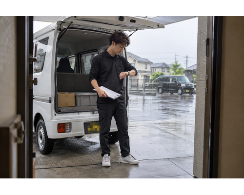 白い軽バンのそばで配送作業をするドライバー