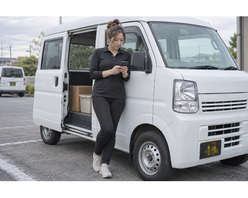 白い軽バンのそばで配送作業をするドライバー