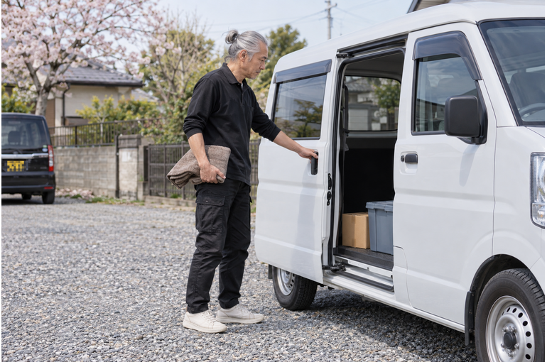 白い軽バンのそばで配送作業をするドライバー
