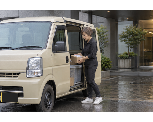 軽バンの荷室で荷物を整える女性ドライバー