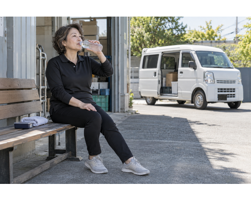 日陰で水分補給をする女性ドライバー