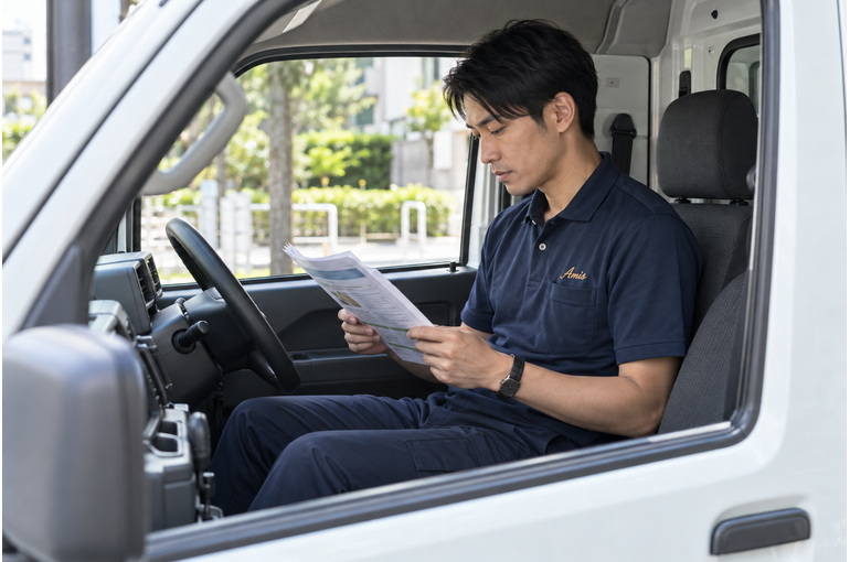 停車した軽バンの運転席で交通ルールの資料を確認する男性