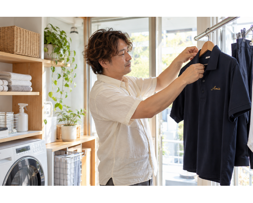 自宅の明るい洗濯スペースで仕事着をハンガーに掛ける男性