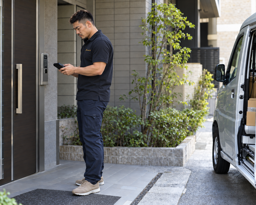 配達先の入口で配送端末を確認する男性
